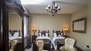 Une chambre d’hôtel avec deux lits, un grand miroir, un lustre et deux fauteuils rembourrés.