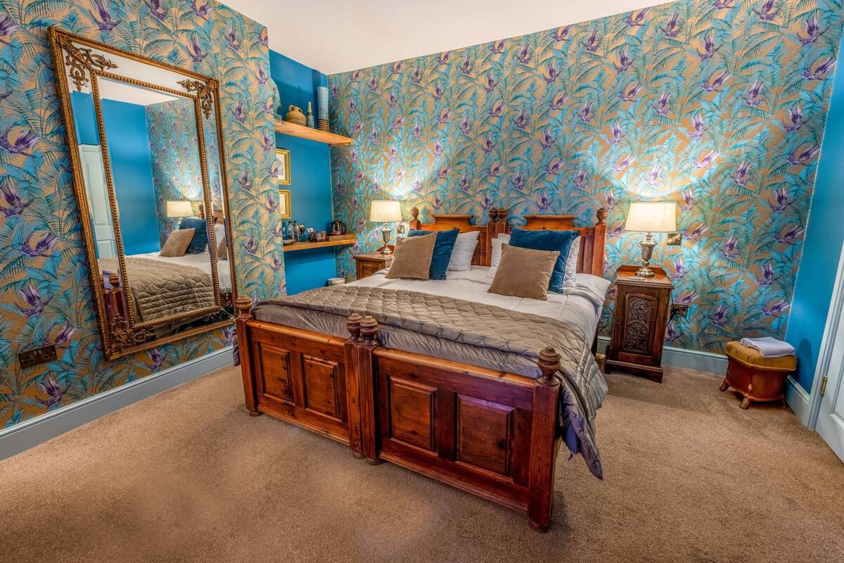 A bedroom with a large mirror, a wooden bed with a quilted headboard, and a patterned wallpaper.