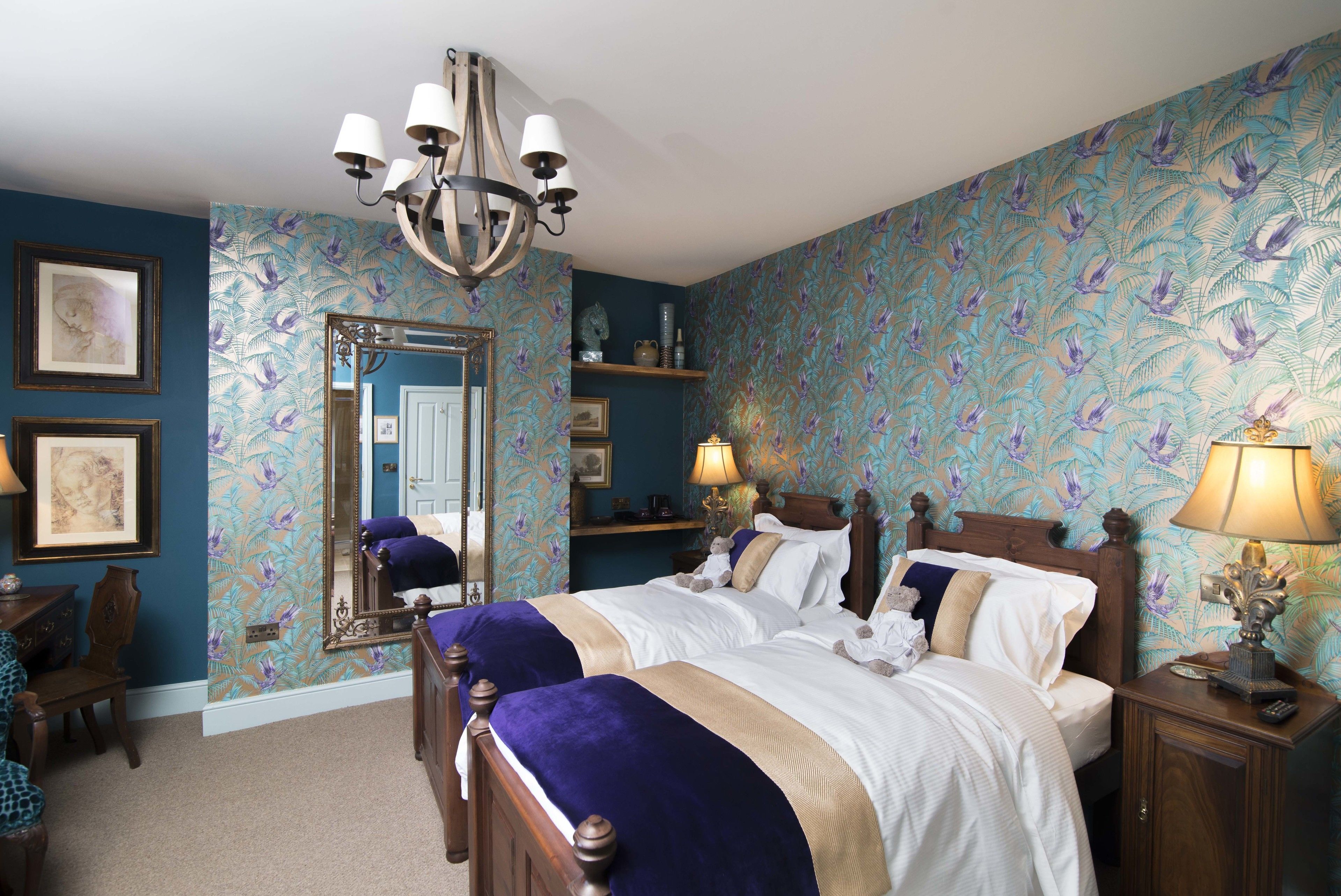 A bedroom with a large bed, a chandelier, a mirror, and a dresser.