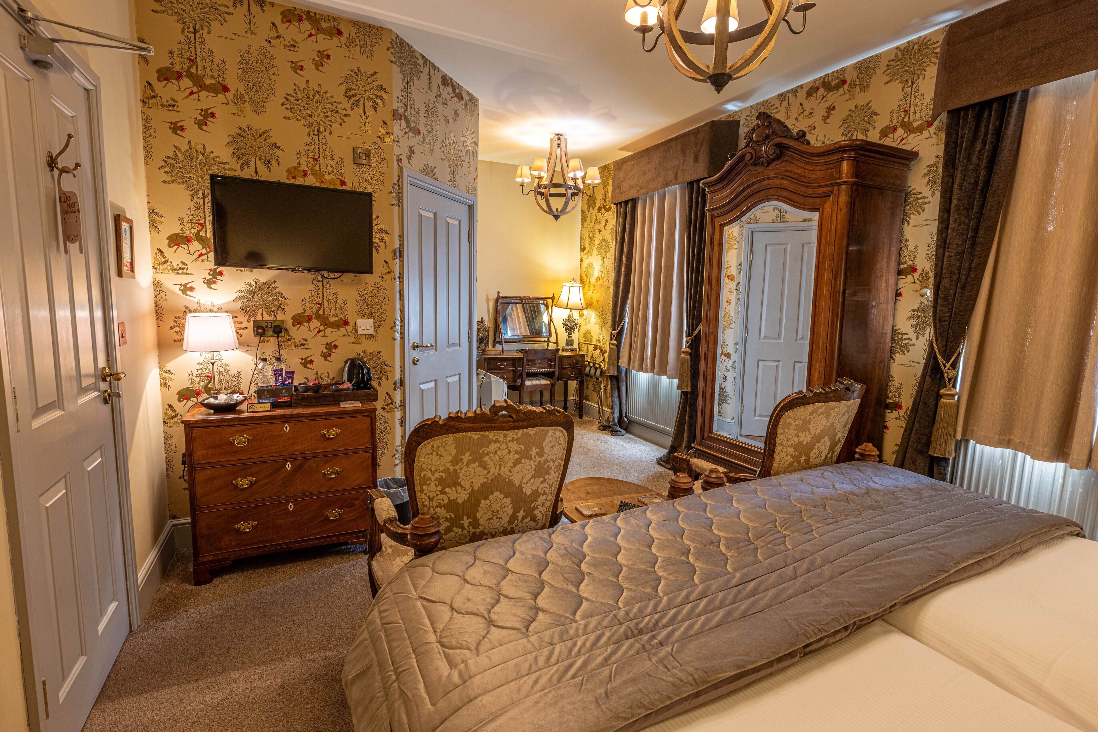 A hotel room with a large bed, a dresser, a chair, a television, and a chandelier.