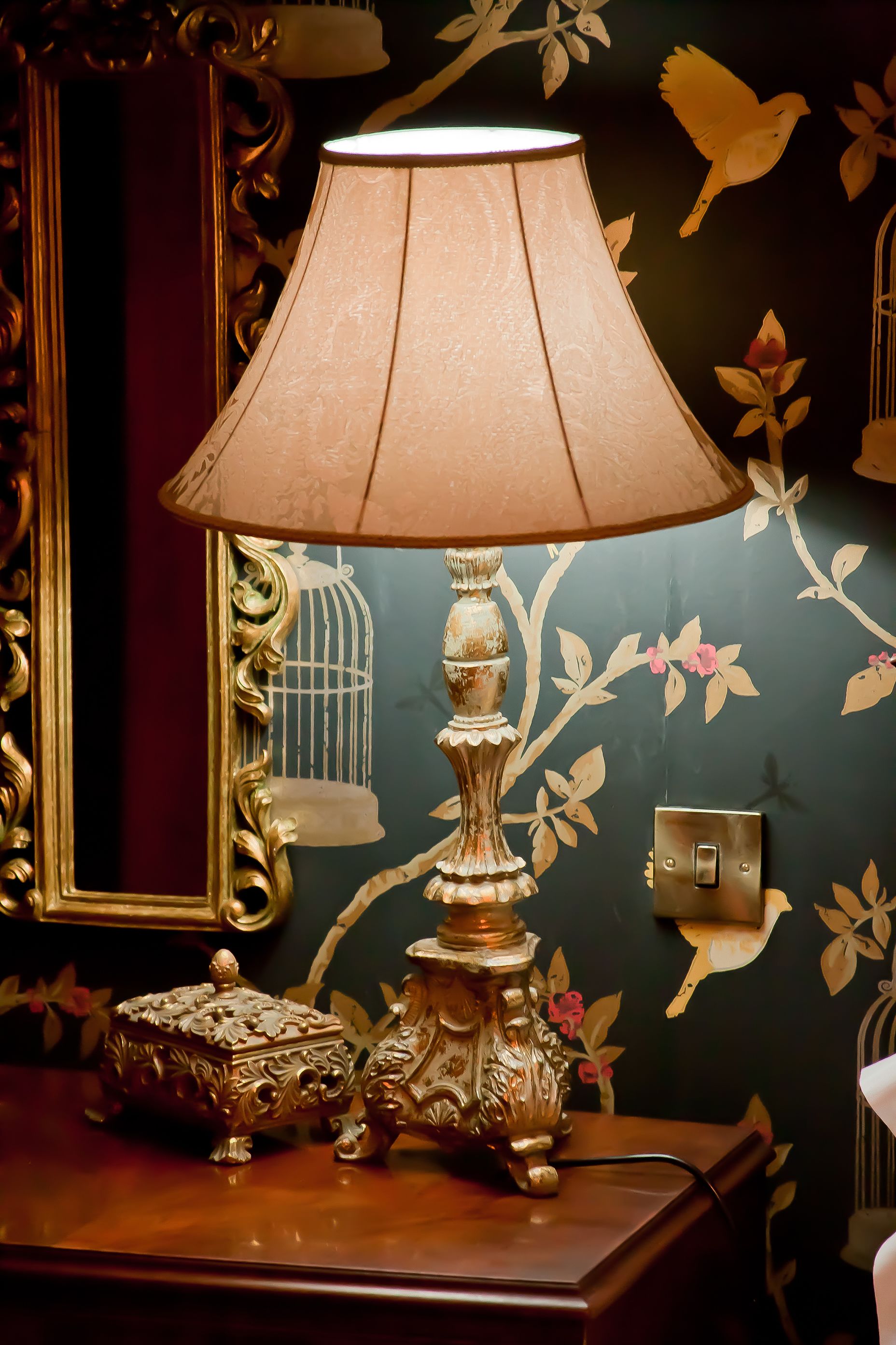 Una lámpara con base decorativa y pantalla iluminada sobre una superficie de madera.