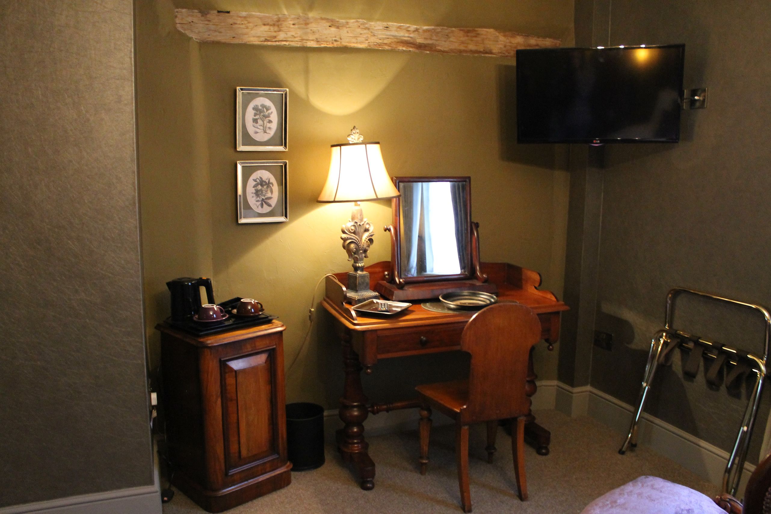 A hotel room with a wooden desk, a chair, a television mounted on the wall, and a mirror.