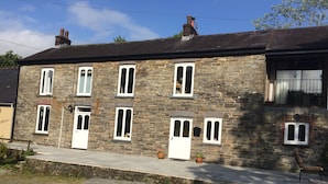 A stone building with multiple windows and doors, a paved front area with potted plants, and a clear sky. - Four Seasons Bed and Breakfast (Carmarthen)