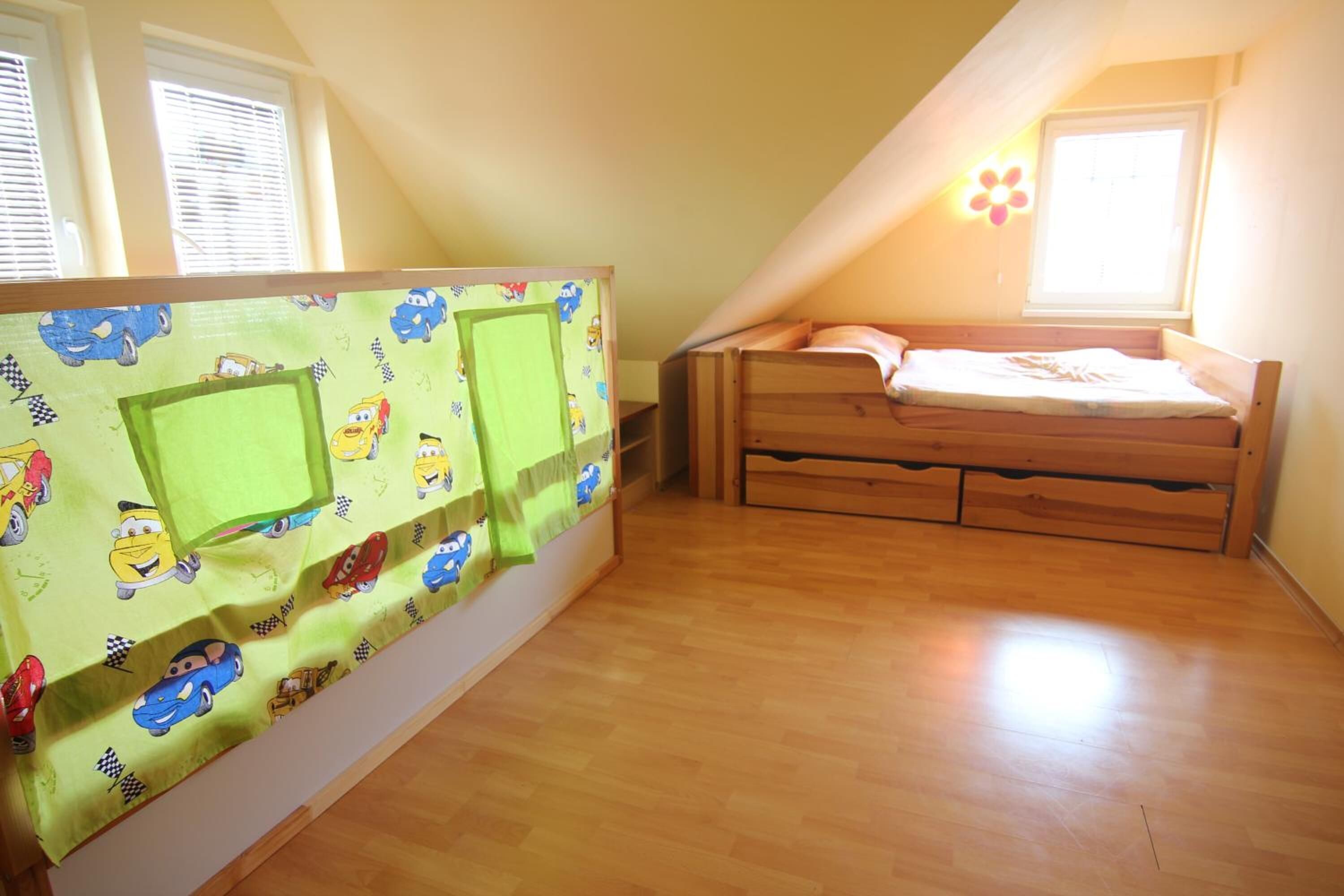 A bedroom with a wooden bed, a green wall with cartoon cars, and a window with blinds.