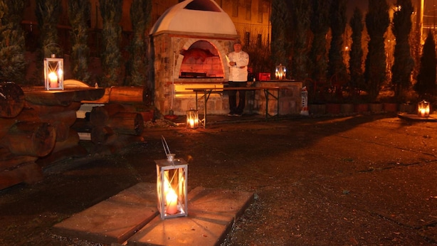 An outdoor brick oven with a chef standing beside it, surrounded by lanterns and logs. - Hotel Restaurant Švejk (Bublava)