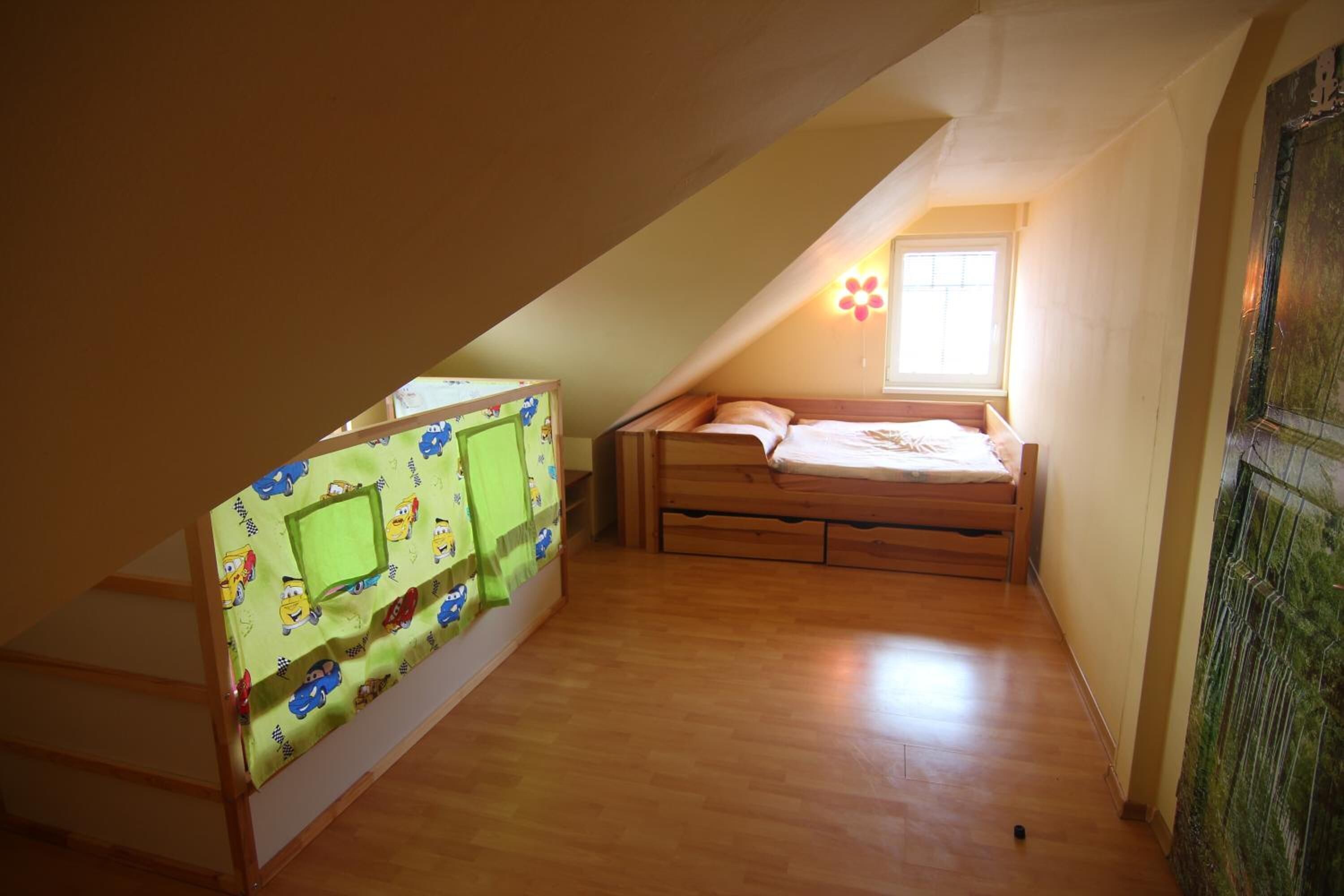 A small attic bedroom with a bunk bed, a window, and a green curtain.