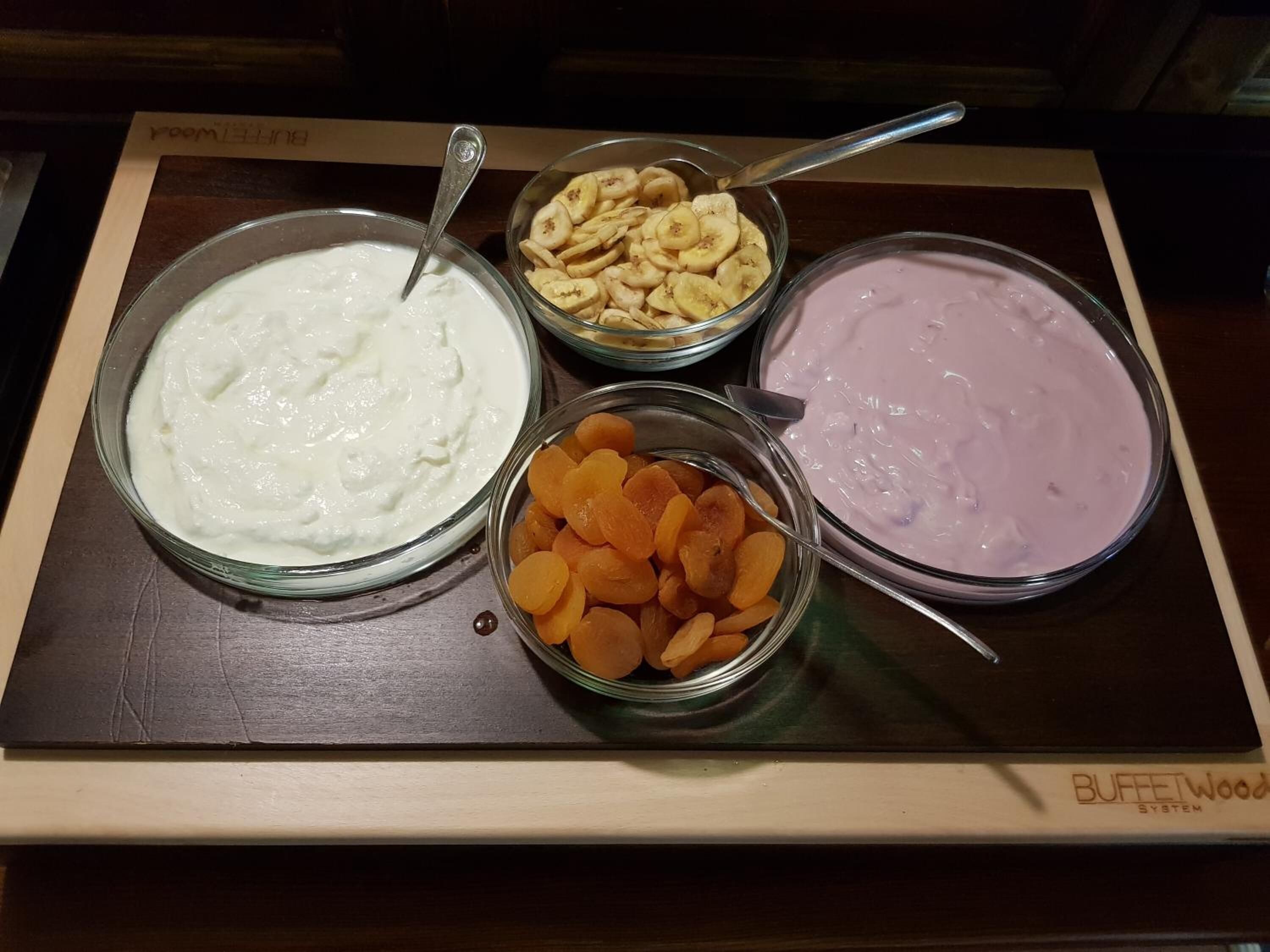 Una mesa de bufé con tres fuentes de comida: una sustancia blanca y cremosa, un tazón con rodajas de plátano y un tazón con albaricoques secos.