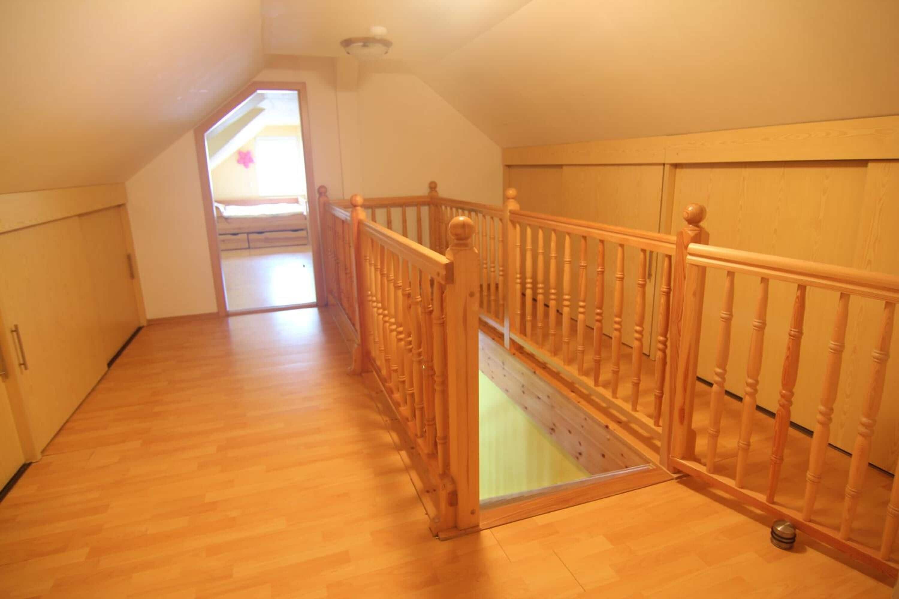 A spacious room with wooden flooring, a wooden staircase with a railing, and a view of a balcony.