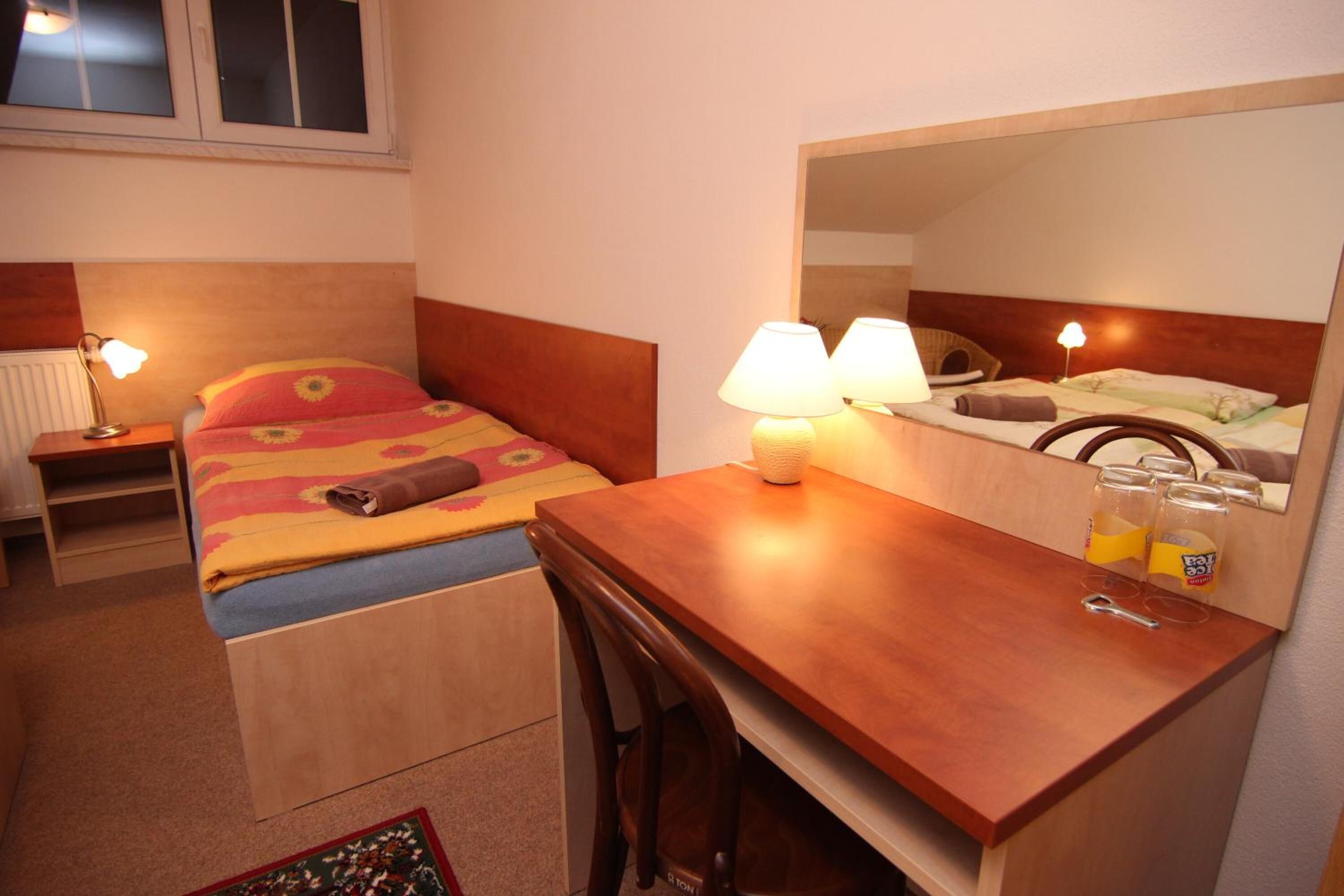 A hotel room with a bed, bedside table, lamp, chair, desk, and a mirror.