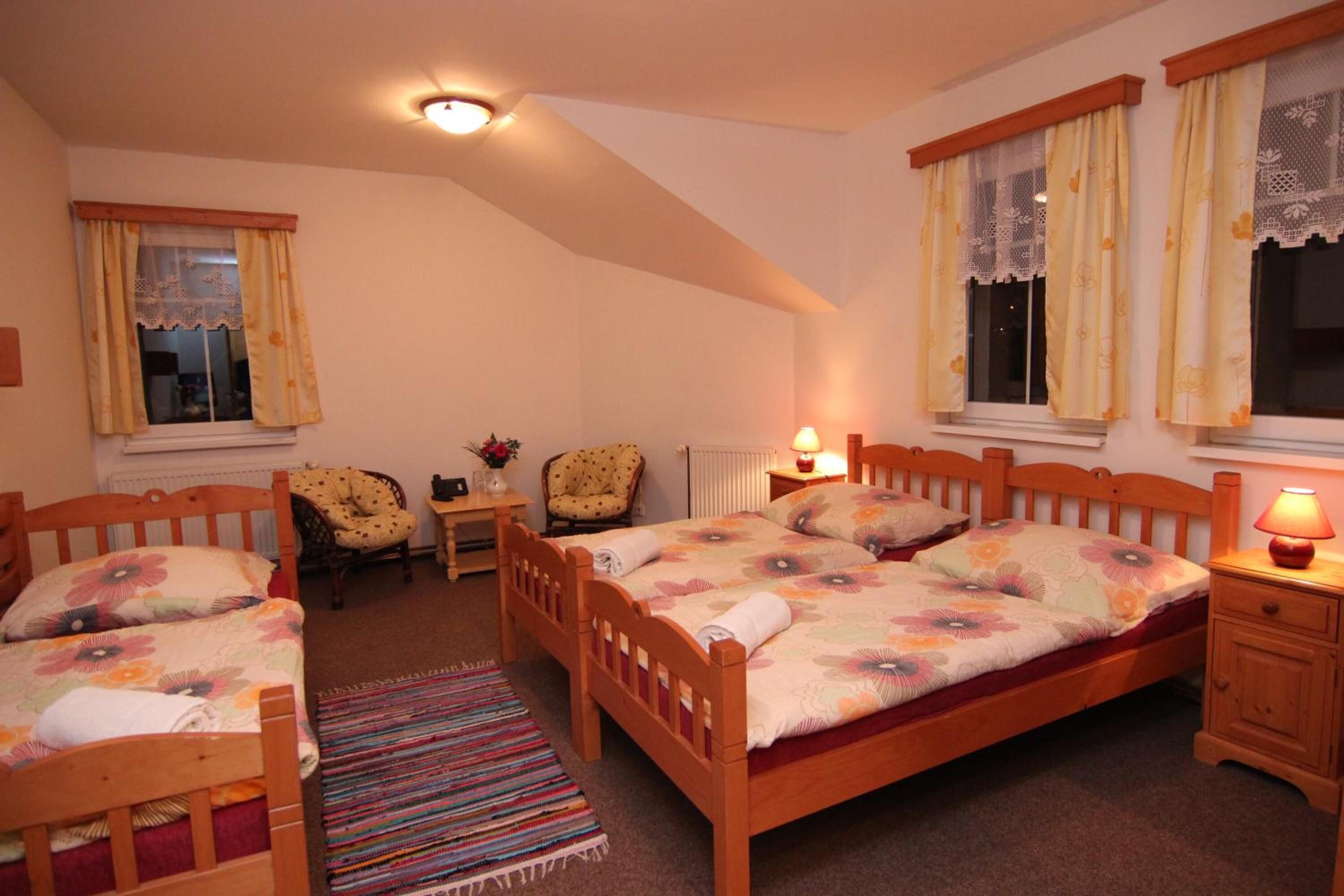 A bedroom with a wooden bed, two chairs, a small table, and a nightstand with a lamp.