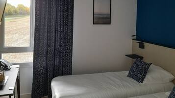 Habitación de hotel con dos camas, un escritorio con teléfono, una ventana con cortinas, un cuadro enmarcado en la pared y una pared de acento azul.