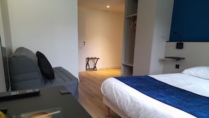 A modern hotel room with a bed, a desk with a computer, a chair, and a small table. - Le Riccoty (Blyes)