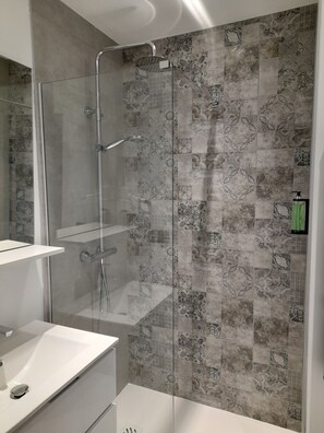 A modern bathroom with a glass-enclosed shower, a white sink, and patterned tiles on the walls.