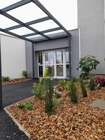 Un edificio moderno con entrada de vidrio, rodeado de un jardín con diversas plantas y flores.