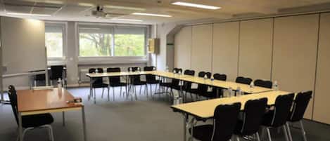 Un salón de conferencias con una larga mesa, sillas negras y una pantalla para proyector.