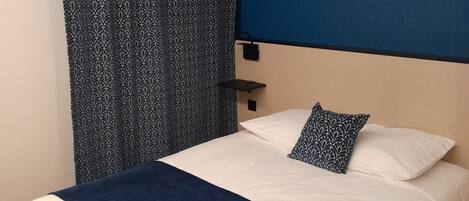 A bedroom with a bed, a blue wall, a leaf-patterned artwork, and a patterned curtain.