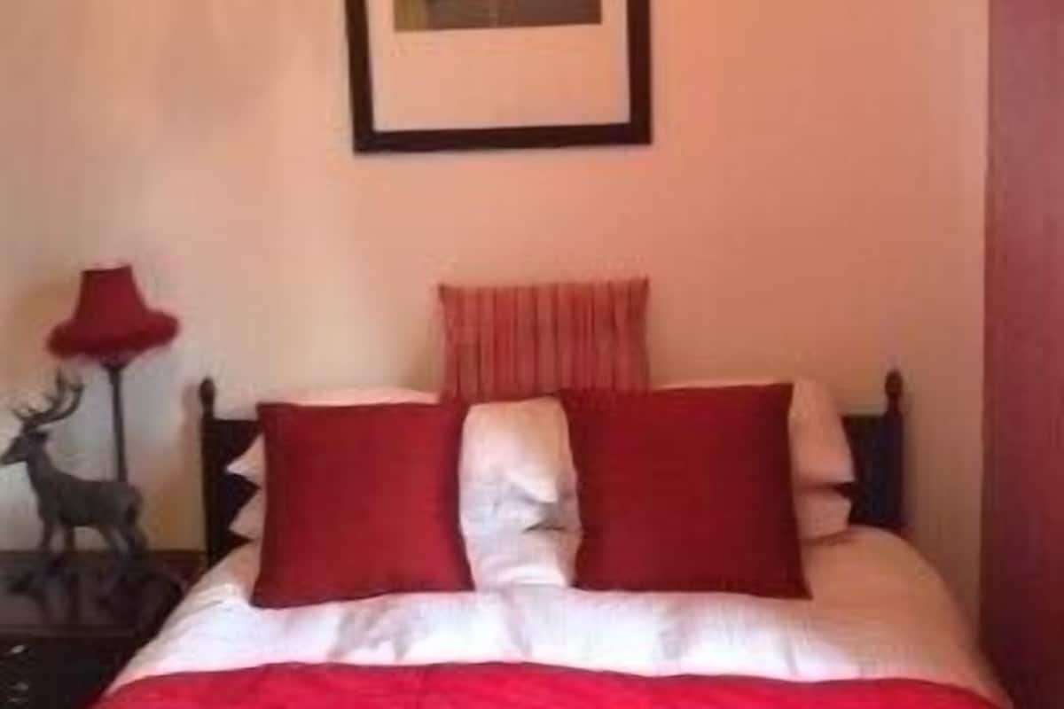 A bedroom with a bed, a framed picture on the wall, and a lamp on a side table.