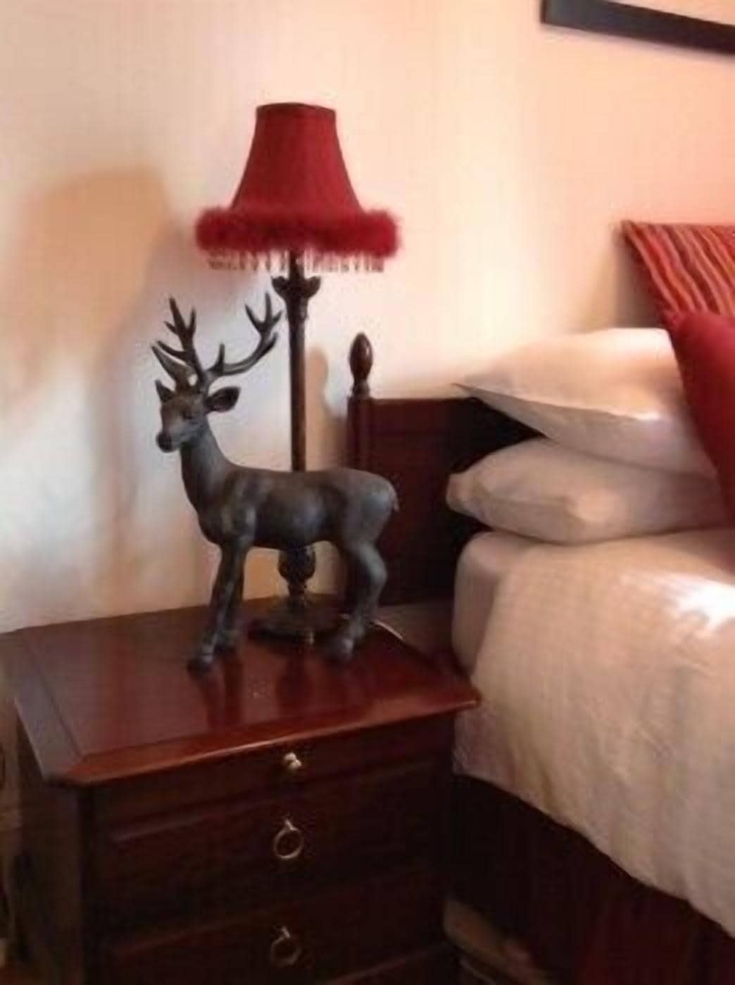 A wooden nightstand with a deer figurine and a red lamp.