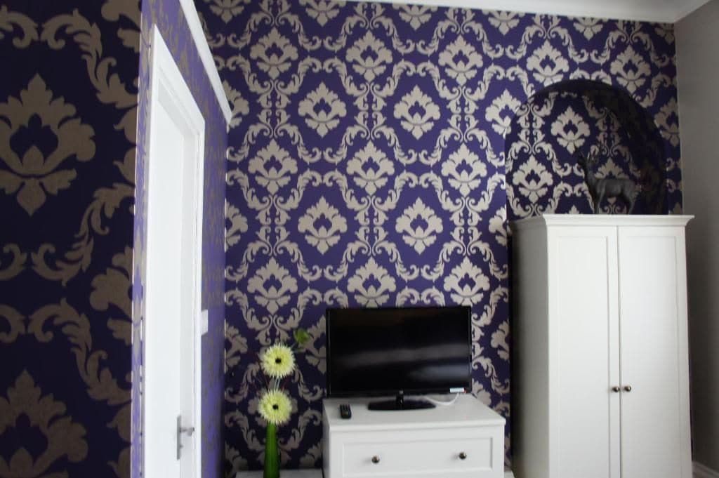 Een kamer met behang met een patroon, een televisie op een standaard, een wit kastje en een deur.