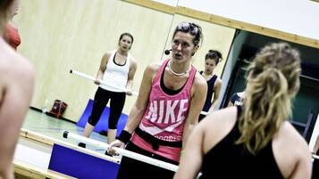 En grupp människor i ett gym med en vägg som består av speglar och en blå matta på golvet.