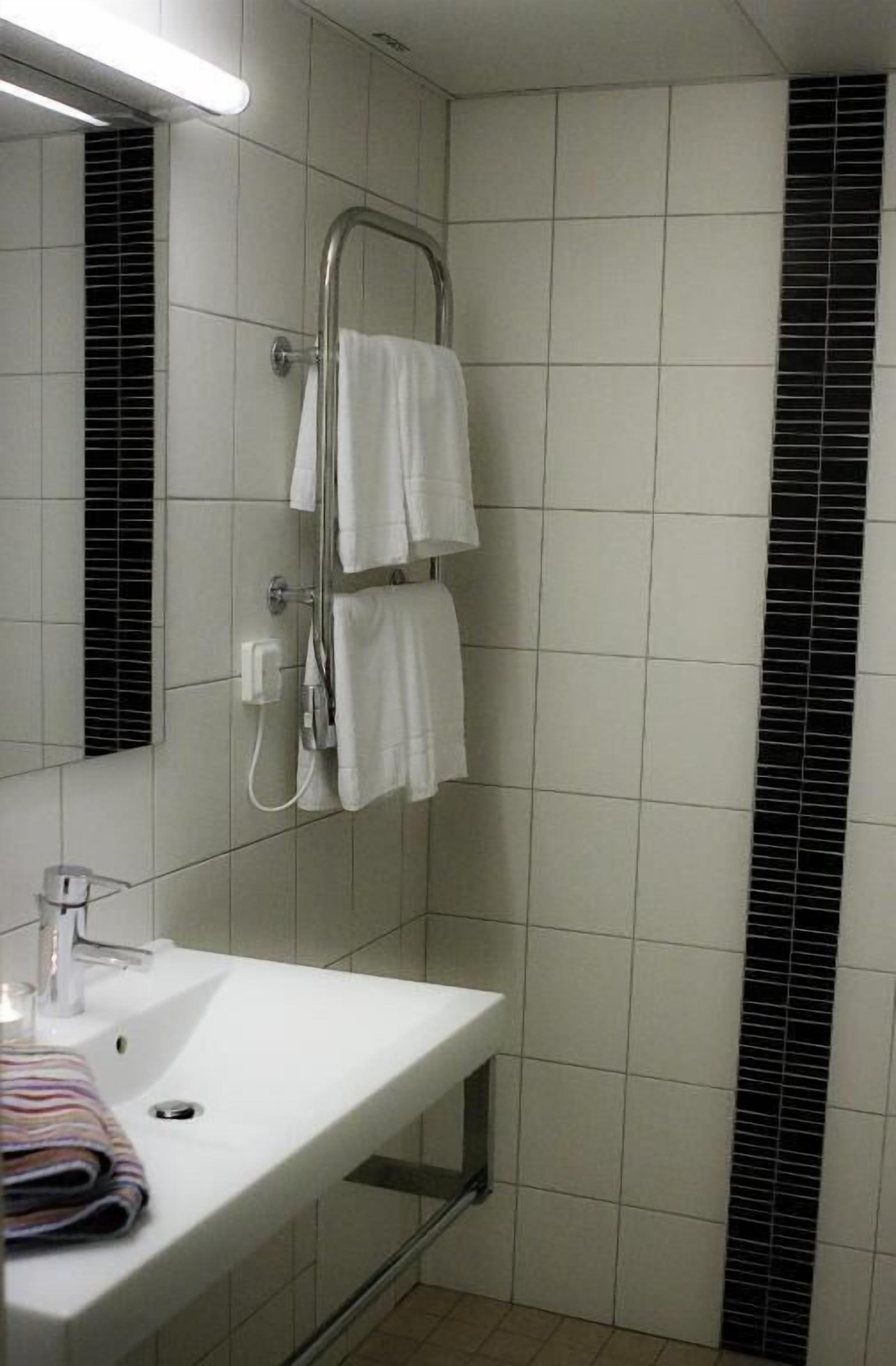 A bathroom with a white sink, a mirror, a towel rack with two towels, and a shower with a glass door.