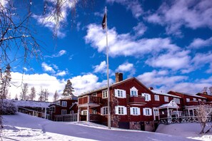 Un edificio de madera roja con varias ventanas y balcones, rodeado de nieve y árboles.