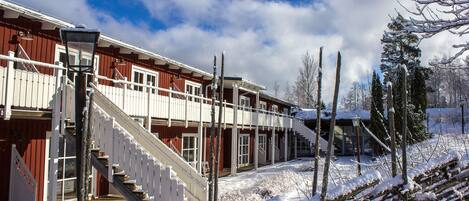 Un edificio rojo con una escalera blanca que conduce a un balcón, rodeado de terreno y árboles cubiertos de nieve.