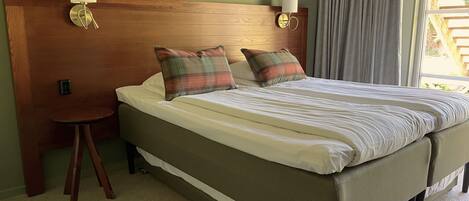Una cama doble con cabecera de madera, dos lámparas de noche y almohadas a cuadros.