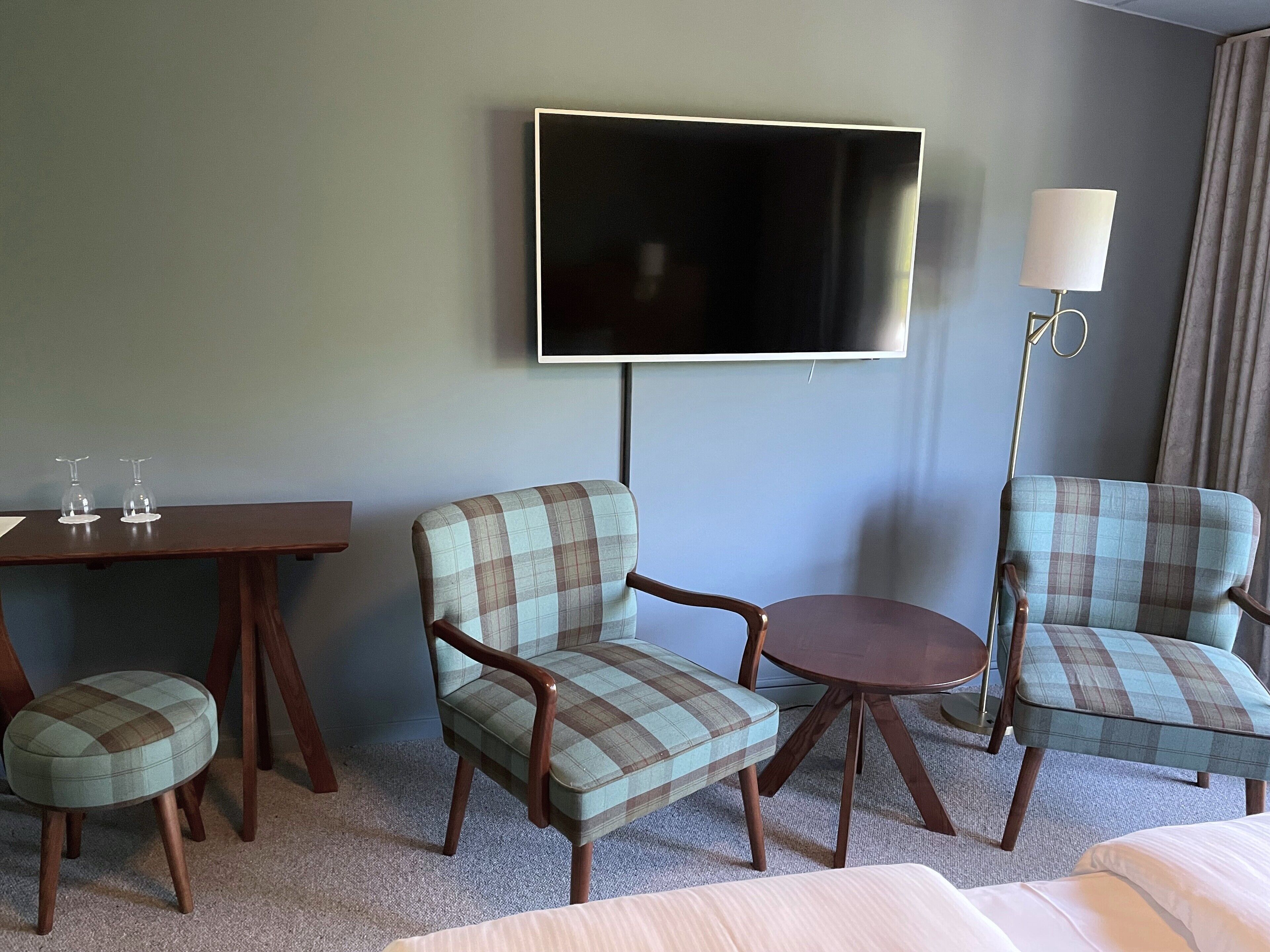 Une chambre d’hôtel équipée d’un téléviseur à écran plat, de deux fauteuils à motifs écossais, d’une petite table ronde et d’un canapé.