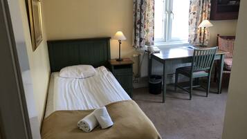 A hotel room with a bed, a desk, a chair, a lamp, and a window with curtains.