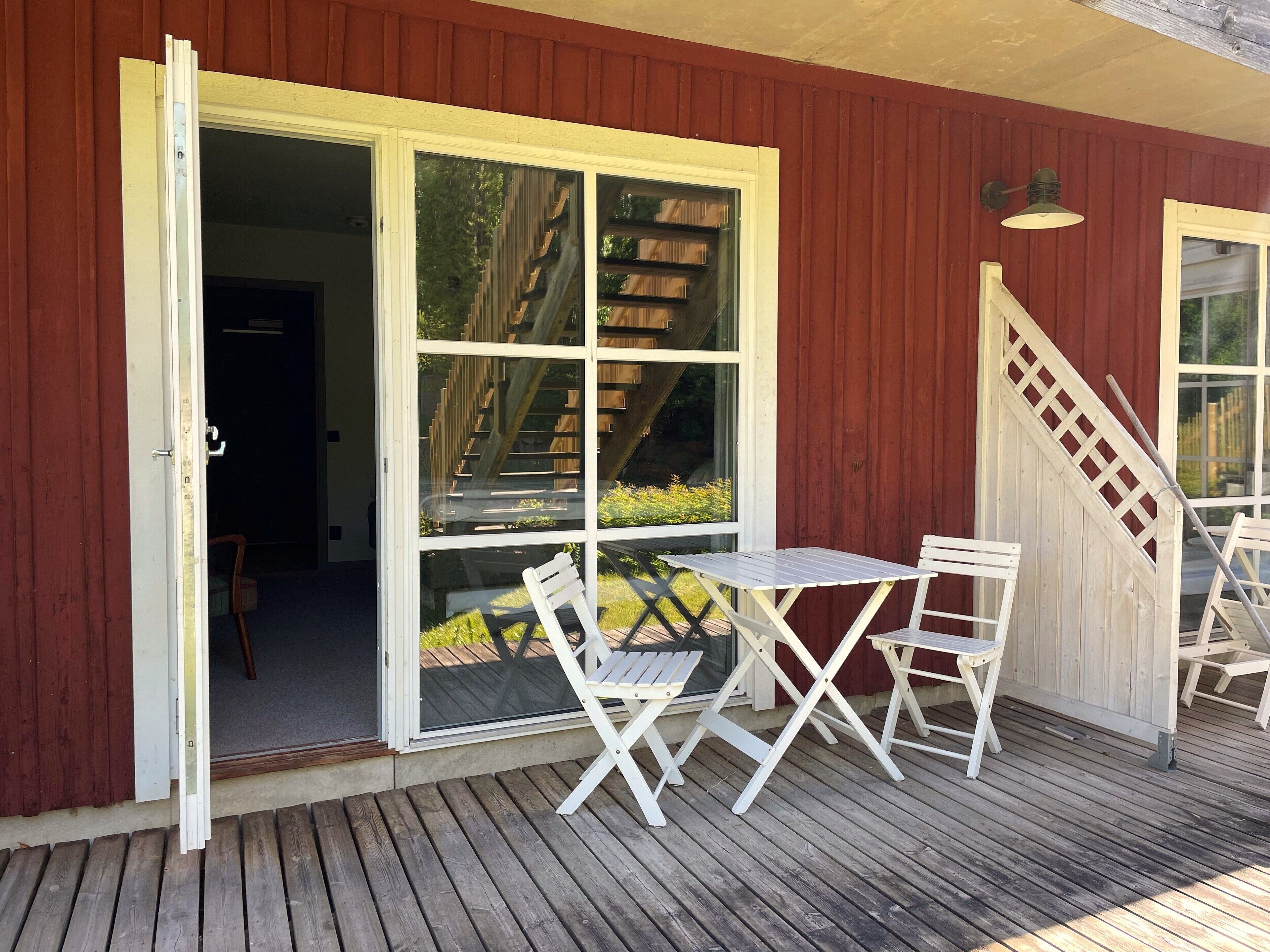 A wooden deck with a table and chairs, a sliding glass door, and a staircase leading to an upper level.