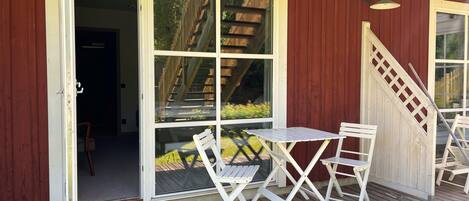 Una terraza de madera con una mesa, sillas, un ventanal corredero y una escalera que sube a un nivel superior.