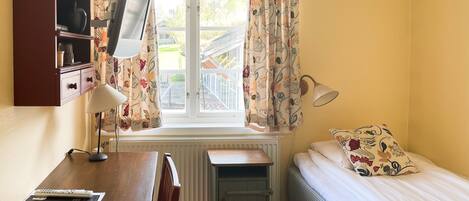 Una habitación con cama, escritorio, radiador, lámpara y cortinas.