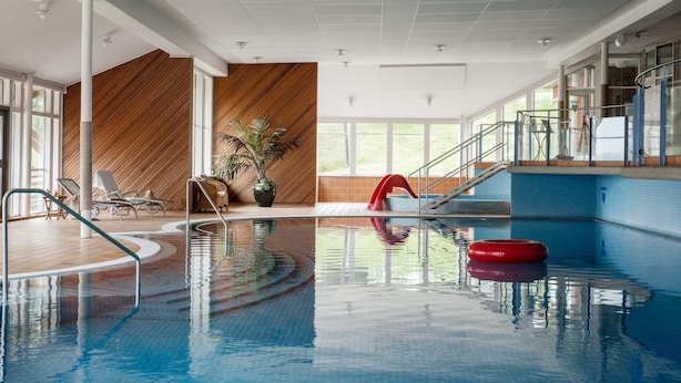 Una piscina interior con agua cristalina, un flotador rojo y una pared de madera con un diseño diagonal.