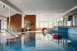 An indoor swimming pool with clear water, a red floating ring, and a wooden wall with a diagonal pattern. - Gyllene Hornet (Tallberg)