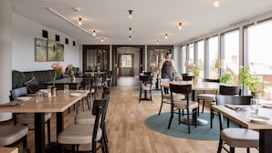 Un comedor moderno con mesas y sillas de madera, un pasillo central y grandes ventanales con vistas.