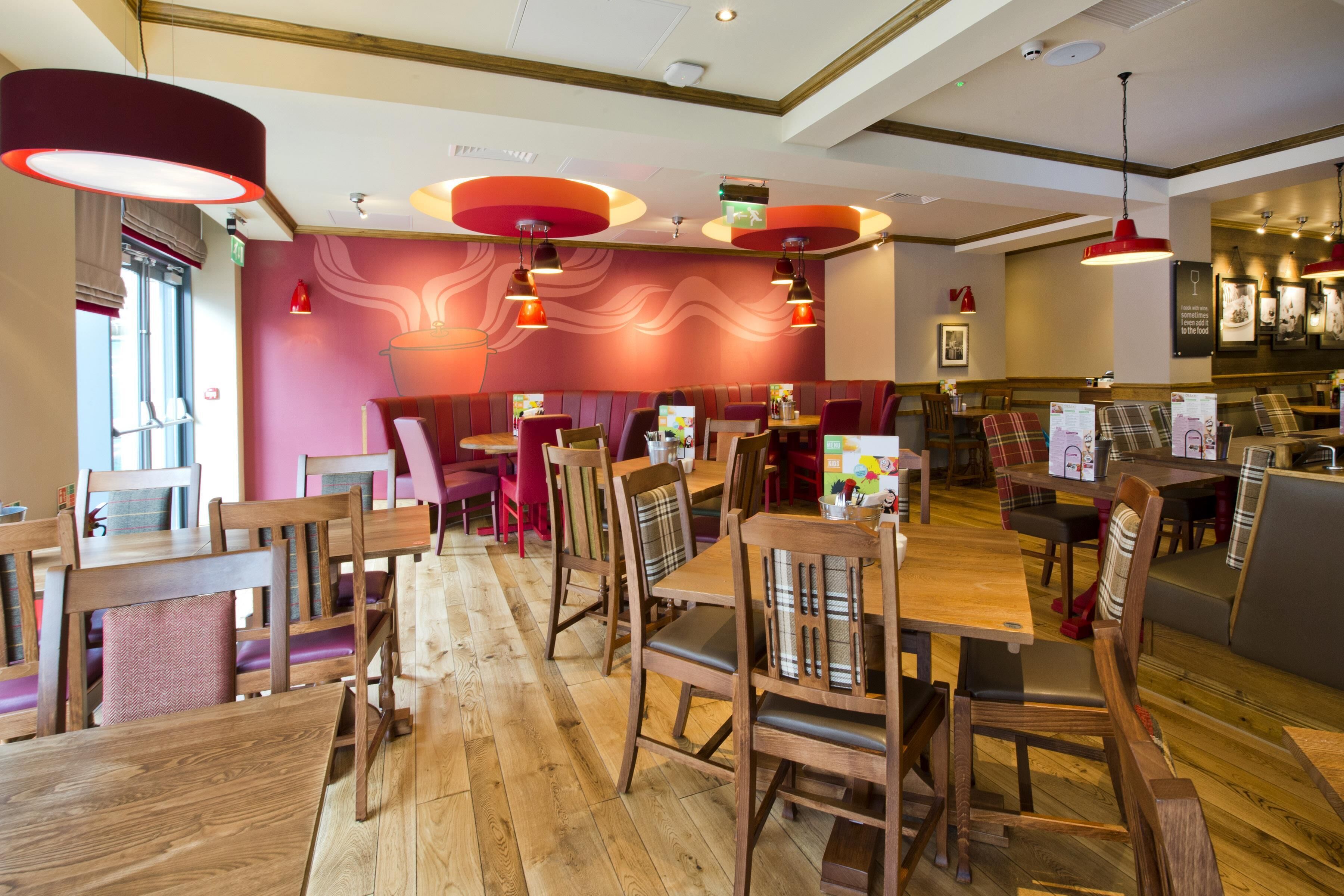 Interior de restaurante con mesas y sillas de madera, iluminación colgante roja y un diseño de pared ondulado.