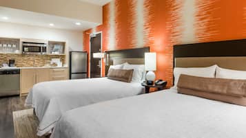 A hotel room with two beds, a kitchenette, and a large orange wall.