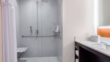 A modern bathroom with a shower, grab bars, a towel rack, and a sink with a mirror.