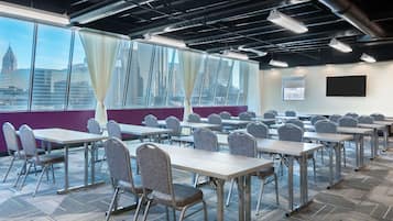A conference room with tables and chairs, large windows with curtains, and a projector screen on the wall.