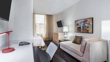 Habitación de hotel con cama, escritorio, silla, sofá, televisor, lámpara y un cuadro en la pared.