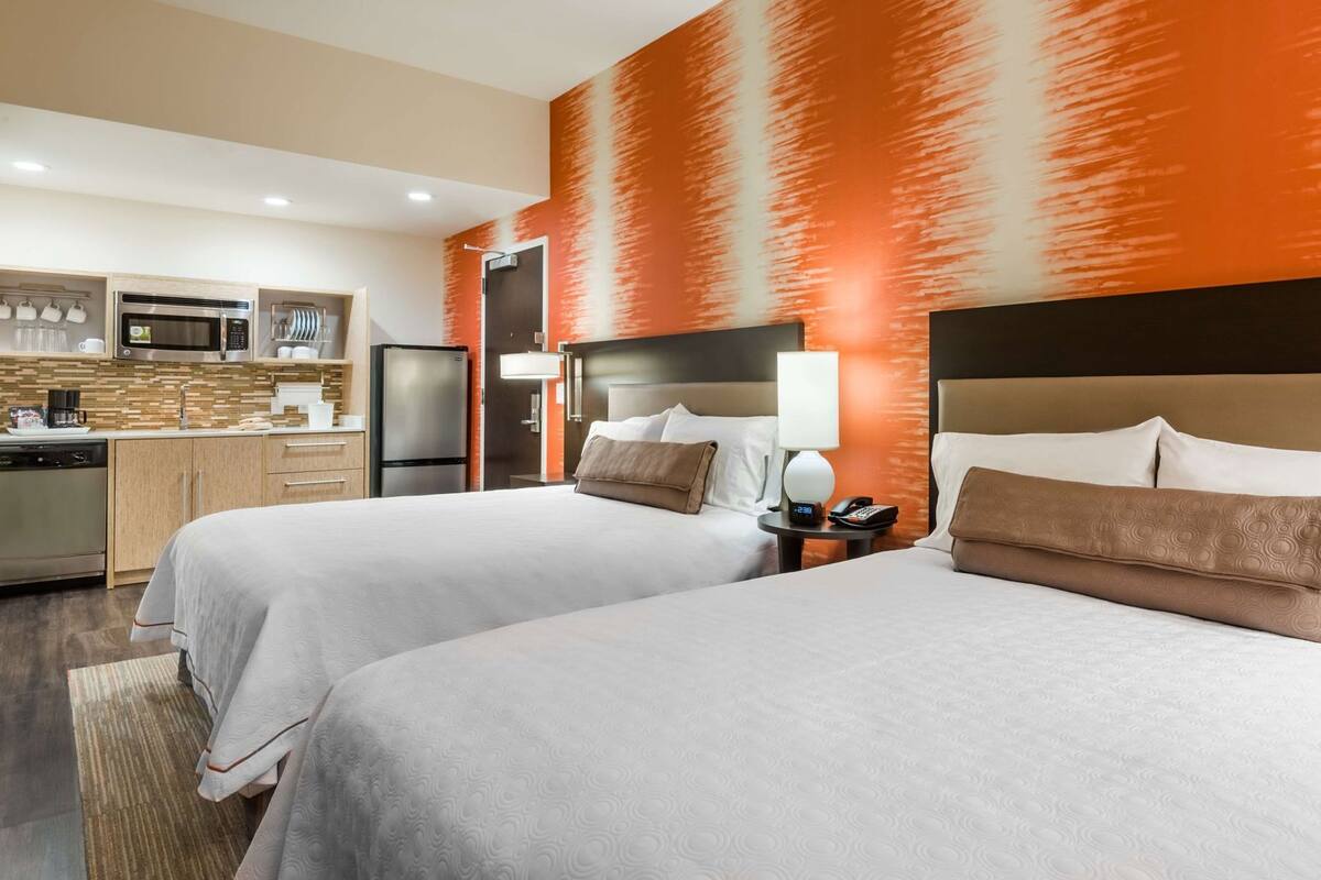 A hotel room with two beds, a kitchenette, and a bathroom.