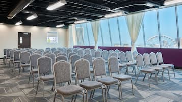 A conference room with rows of chairs, large windows with curtains, and a view of a Ferris wheel.