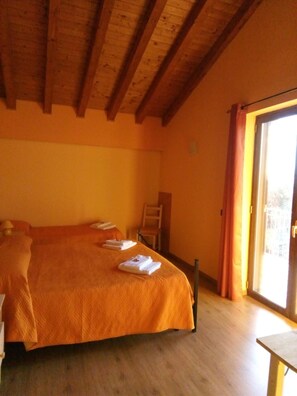 A bedroom with a large bed, wooden beams on the ceiling, a chair, and a sliding glass door to the right. - Aurora dell'Etna (Zafferana Etnea)