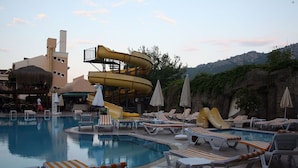 A pool area with lounge chairs, umbrellas, and a water slide.