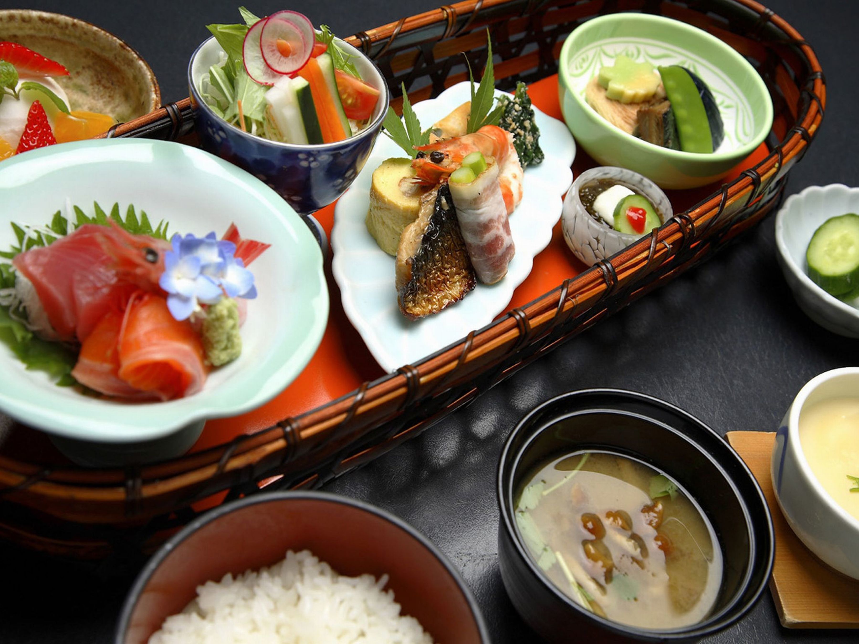 Erilaisia japanilaisia ruokia, kuten sushia, sashimia ja keittolajeja, on aseteltu puiselle tarjottimelle.