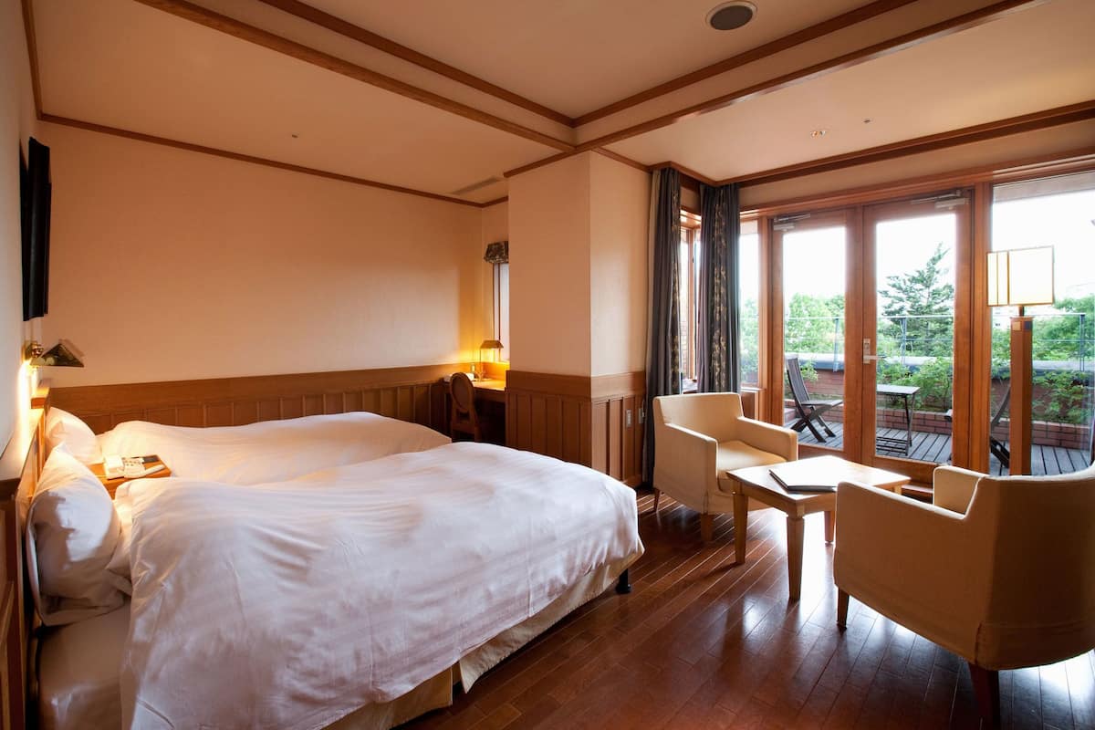 Ein Hotelzimmer mit einem großen Bett, einem Schreibtisch und einem Stuhl. Ein Fenster bietet Blick auf die grüne Umgebung.