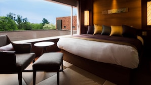Ein Hotelzimmer mit einem großen Bett, einer Sitzecke mit Sesseln, einem kleinen Tisch und Blick ins Freie.
