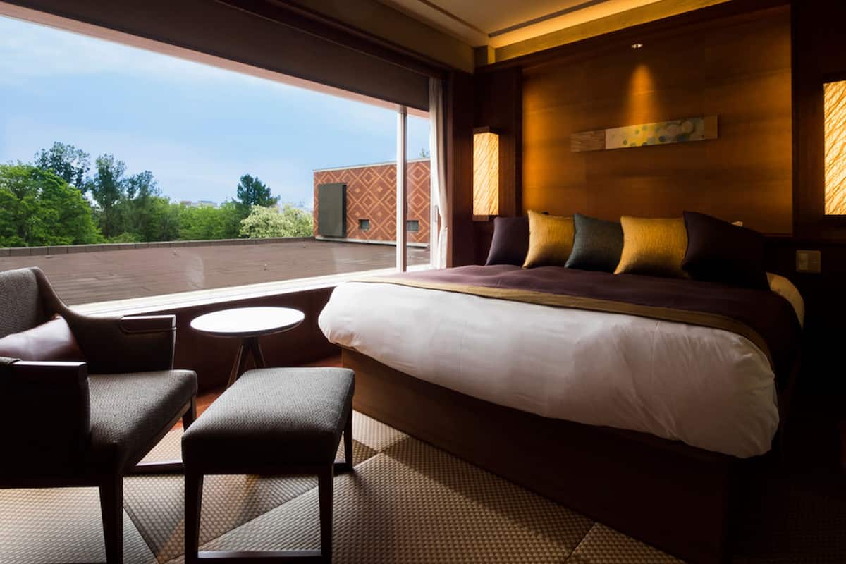 Ein Hotelzimmer mit einem großen Bett, einer Sitzecke mit Sesseln, einem kleinen Tisch und Blick ins Freie.