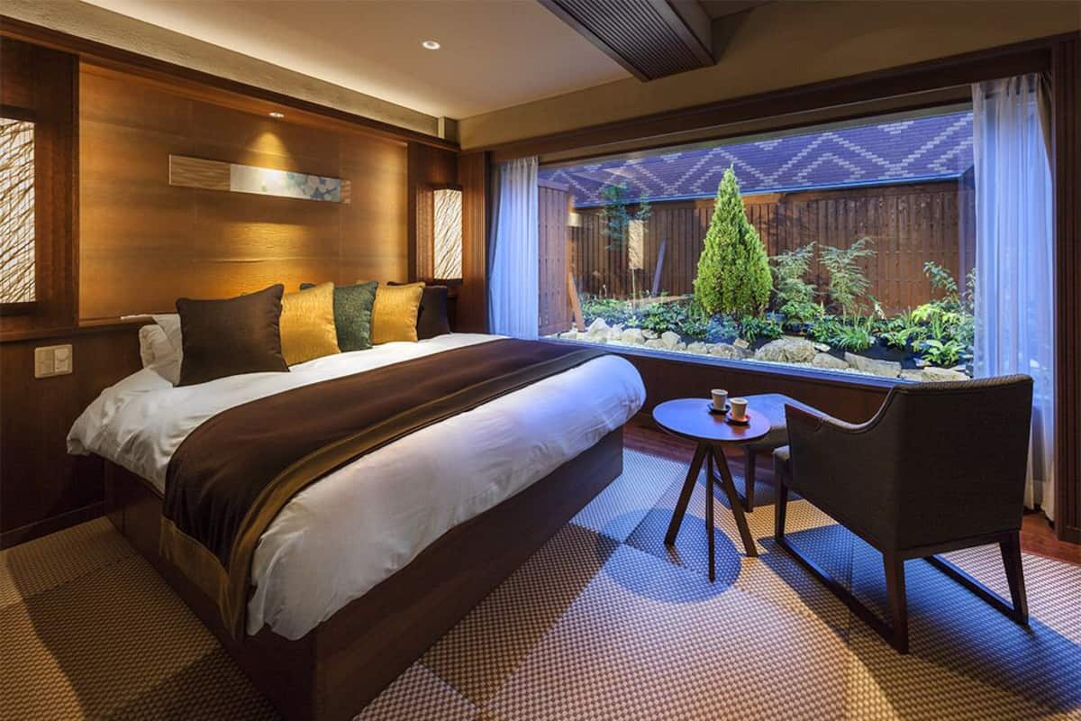 Ein Hotelzimmer mit einem großen Bett, einem kleinen Tisch und einem Stuhl. Es gibt ein Fenster mit Blick auf einen Garten.